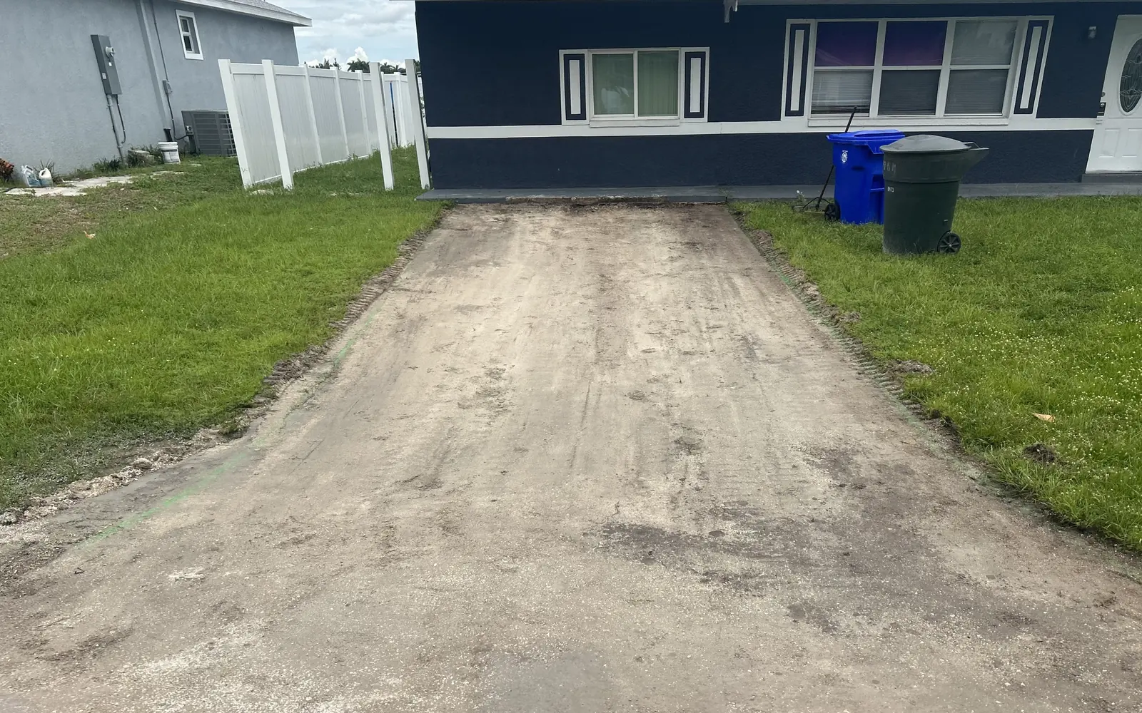 Before: a bare sand and dirt driveway in front of a navy blue stucco house